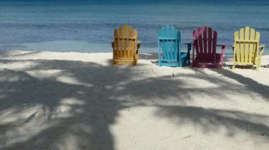Palm Beach Aruba 'da renkli sandalyeler. Plajda palmiye ağacı yansıması var.