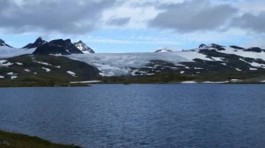 Norveç 'in Jotunheimen Ulusal Parkı' ndaki karlı dağların önündeki göl.