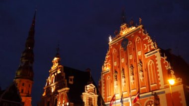 Geceleyin Riga Letonya 'da St. Peter Kilisesi' nin arka planında Kara Kafalar Evi.