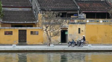 Bisikletli Vietnamlı kadınlar Hoi An Vietnam 'daki nehir cephesinden geçiyorlar.