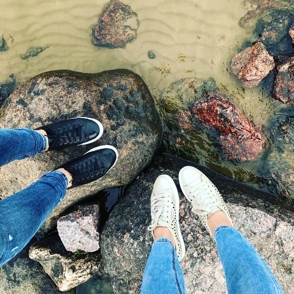 Pernas em tênis e jeans ficar em pedras na água . — Fotografia de Stock