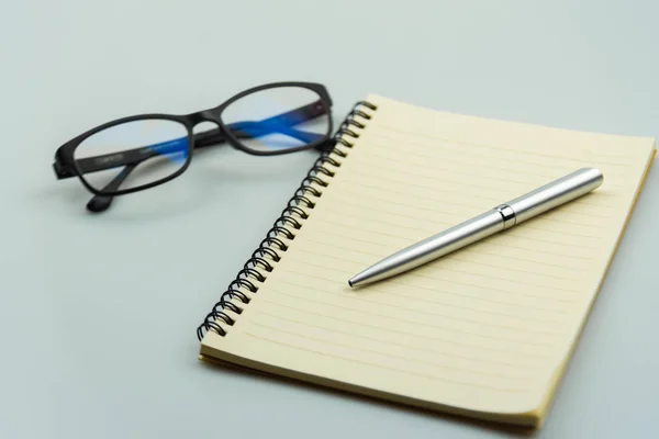 Notebook, caneta e óculos sobre fundo cinza — Fotografia de Stock