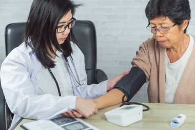 Doktor gri arka plandaki yaşlı kadını kontrol ediyor.