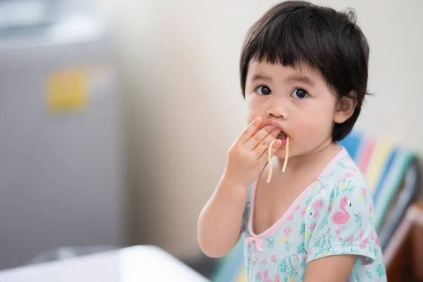 Güzel Asyalı bebek yemek odasında spagetti yiyor.