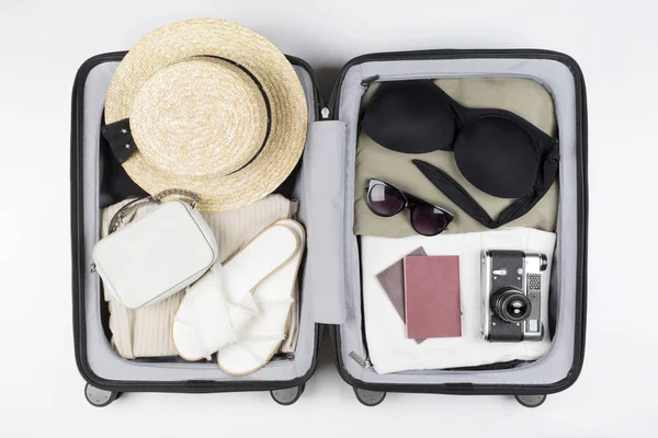 Open suitcase packed for travelling. Hat, glasses, sandals, swimsuit, bag, passport