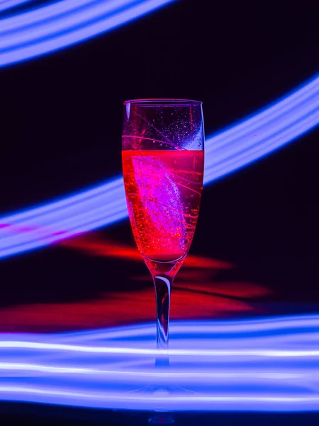 红色的香槟酒杯 背景是黑色的 其效果是在长时间的快门速度上画出蓝光 用霓虹灯装饰聚会或假日的概念 — 图库照片