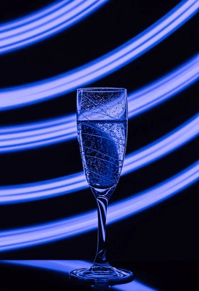在黑色背景上的一杯香槟 其效果是在长时间的快门速度上画出蓝光 装饰具有霓虹灯效果的聚会或假日的概念构想 — 图库照片
