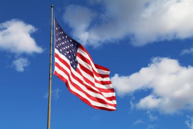 Güneşli bir günde birkaç beyaz bulutla dalgalanan parlak bir Amerikan bayrağı.