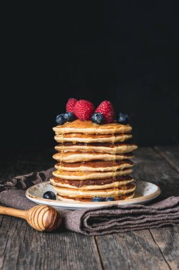 Stack of pancakes with honey and fresh berries on wooden table clipart