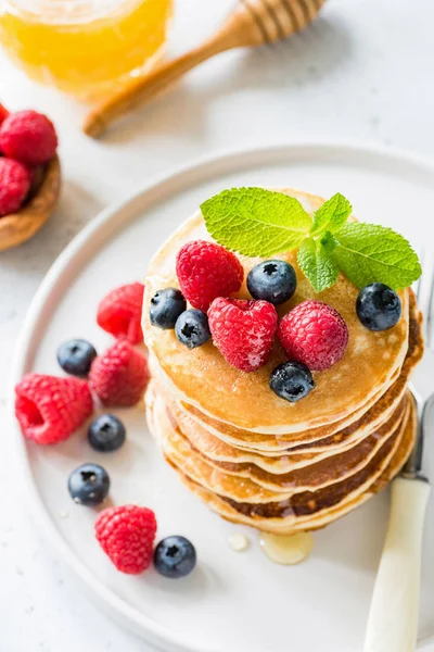 Млинці зі свіжими ягодами та медом на білій тарілці — стокове фото
