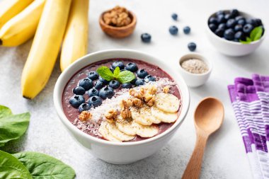 Beton zemin üzerine superfood Topingler ile Acai smoothie kase. Mor smoothie muz, chia tohum, Hindistan cevizi, ceviz ve yaban mersini ile beyaz kase. Vegan, sağlıklı beslenme, sağlıklı yaşam konsepti