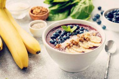 Acai smoothie kase gri beton zemin üzerine. Superfood Topingler muz, ceviz, Hindistan cevizi, chia tohum ve taze yaban mersini ile güler yüzlü. Seçici odak