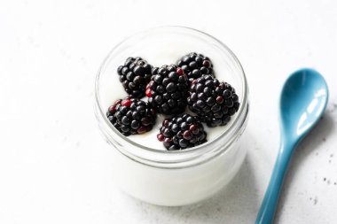 Yunan yoğurt ve taze böğürtlen beyaz beton zemin üzerine bir kavanoza. Closeup görünümü, seçici odak