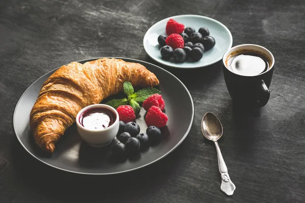 Kruvasan, çilek, reçel ve kahve siyah masada kahvaltı kavram Fransız. Tonlu görüntü