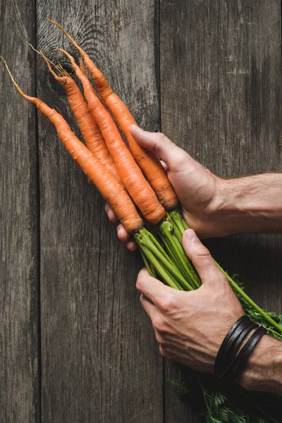 Zanahorias en las manos de los agricultores sobre fondo de madera —  Fotos de Stock