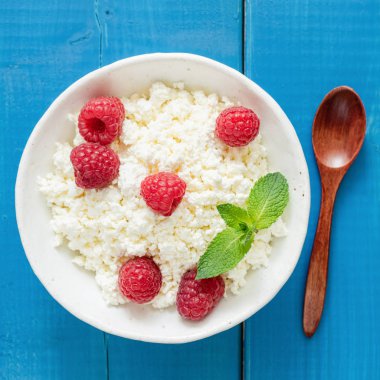 Lor peyniri, çiftçi peynir, ricotta veya kase taze ahududu mavi ahşap zemin üzerine tvorog. Sağlıklı yaşam, diyet, fitness kavramı