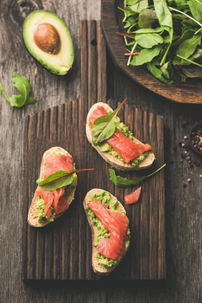 Tostadas de salmón con aguacate en tabla de cortar de madera, vista superior — Foto de Stock