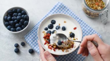 Woman mixing yogurt with granola and berries, healthy breakfast food. Clean eating concept