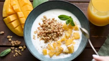 Mango ve tahıl gevreğiyle yoğurt yiyorum. Üst manzara, ahşap masa arkası. Sağlıklı beslenme kavramı, sağlıklı yaşam tarzı