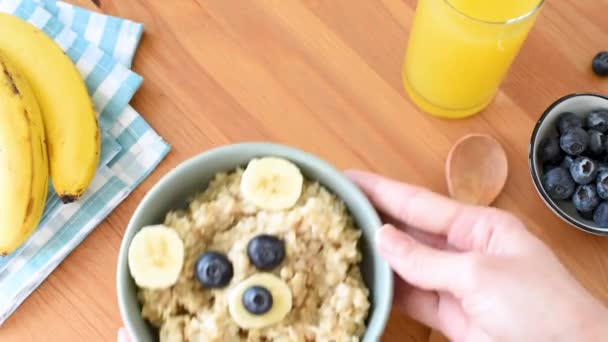 女人把早餐燕麦碗放在桌上 健康的食物 有趣的食物艺术为孩子们 用水果和浆果做成的可爱的泰迪熊脸 — 图库视频影像