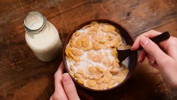 牛乳でコーンフレークを食べる 朝食シリアルコーンフレークのボウルを食べる女性の手のトップビュー 素朴な木製のテーブルの背景 — ストック動画