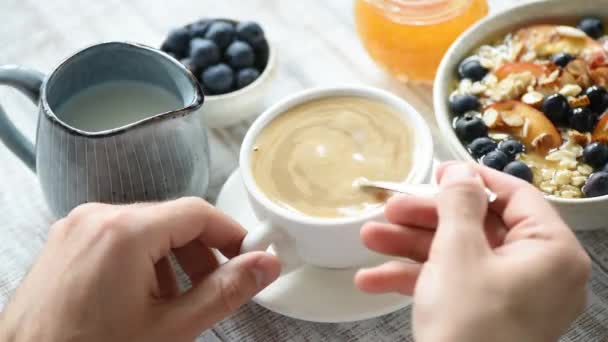 若い男性の手は 白いカップ スローモーションでクリームとコーヒーを混合します 健康的な朝食テーブルのセットアップ — ストック動画