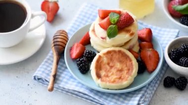 Syrniki veya taze çilek, böğürtlen, bal ve yan tarafta siyah kahve fincan ile süzme peynir krep. Lezzetli sağlıklı kahvaltı görüntüleri