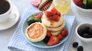 Taze çilek, böğürtlen ve kahve ile servis edilen süzme peynir krep üzerine dökülen balın yakından görünümü. Lezzetli kahvaltı görüntüleri
