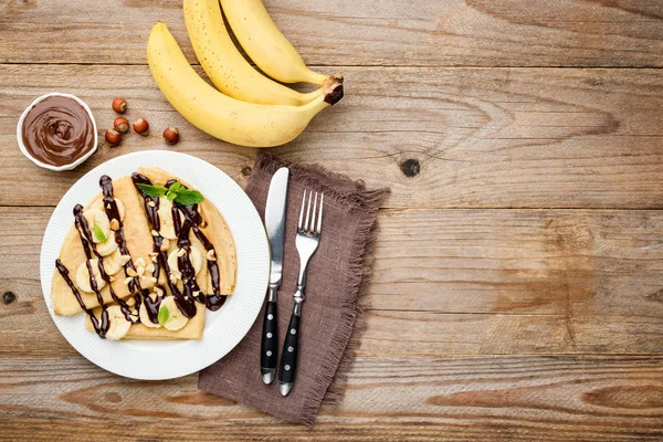 Crepes with chocolate sauce and banana on white plate