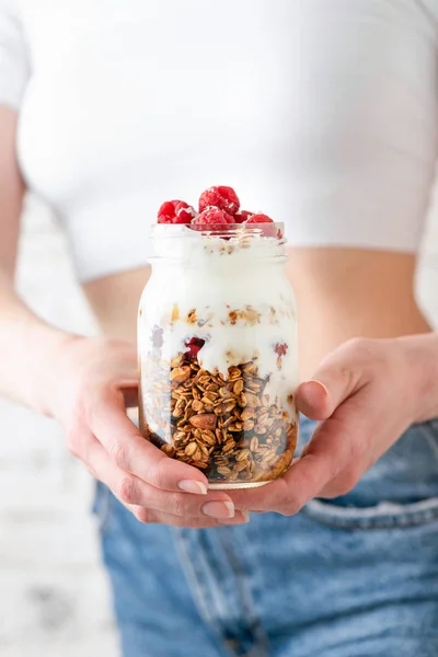 Woman holding jar of yogurt with raspberry and oat granola