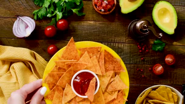 黄色いプレート 木製のテーブルの背景にトマトソースとサルサとトルティーヤチップス メキシコ料理の前菜プレート トップビュー — ストック動画