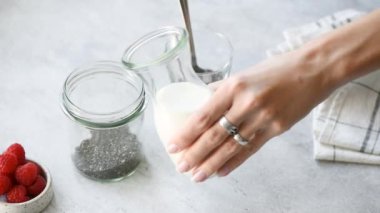 Chia puding adım adım tarifi. Kadın eli chia tohumu ile kavanoza badem sütü ekleyin. Sağlıklı vegan ve vejetaryen gıda