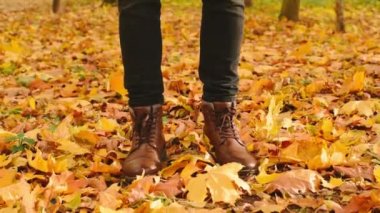 Sonbahar parkında deri çizmeli bir adam akçaağaç yapraklarının üzerinde duruyor. Mevsimlik sonbahar arkaplan görüntüleri tam HD