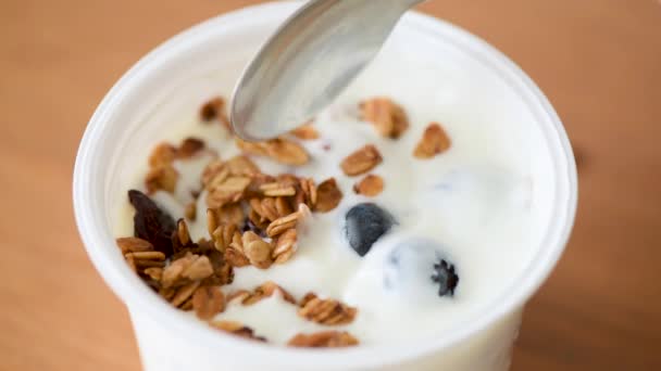 Personne qui mange du yaourt avec du granola et des bleuets dans un pot en plastique. yaourt grec petit déjeuner ou collation. Alimentation propre, concept alimentaire végétarien 
