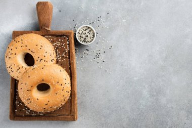 Gri beton arka planda iki susamlı simit, metin ya da tasarım için üst görünüm kopyalama alanı. Taze pişmiş Amerikan simidi.