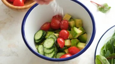 Sebze salatasına tuz ekliyorum. Kirazlı domates, salatalık ve avokado salatası. Sağlıklı vejetaryen yemekleri hazırlıyorum.