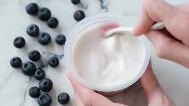蓝莓希腊酸奶在罐子里 人们用天然的希腊酸奶在塑料瓶中搅拌蓝莓馅 商店购买蓝莓酸奶 — 图库视频影像