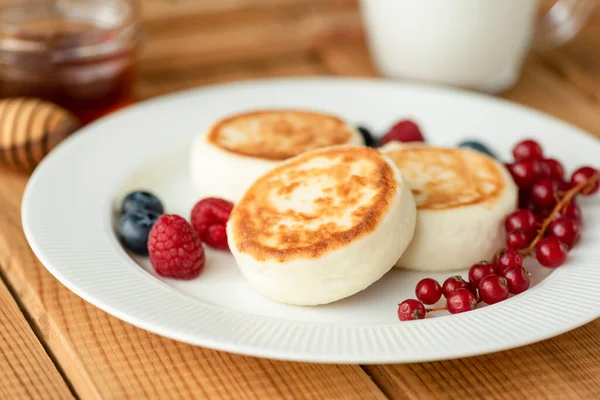 西尔尼奇奶酪煎饼 白盘上有夏天的浆果 木制桌子背景 俄罗斯甜早餐奶酪煎饼 — 图库照片