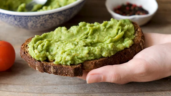 Rye bread toast with mashed avocado. Healthy vegan vegetarian breakfast or snack food. Avocado toast in hand