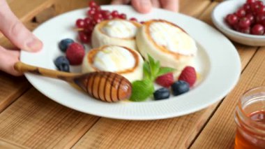 Süzme peynir, ekşi krema, bal ve böğürtlenli Syrniki böreği. Erkek elleri peynirli börek servis ediyor, lezzetli tatlı kahvaltı yemekleri.