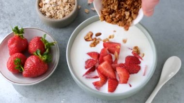 Çilekli yoğurt ve granola. Kahvaltılık gevreğin yavaşça çilekli yoğurda dökülmesi. Temiz yeme, sağlıklı yeme ve sağlıklı yaşam tarzı kavramı