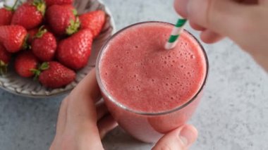 Bardakta taze çilekli smoothie ve pipet. Erkek eller taze vejetaryen içeceğini pipetle karıştırır, yakın çekim görüntüsüyle.