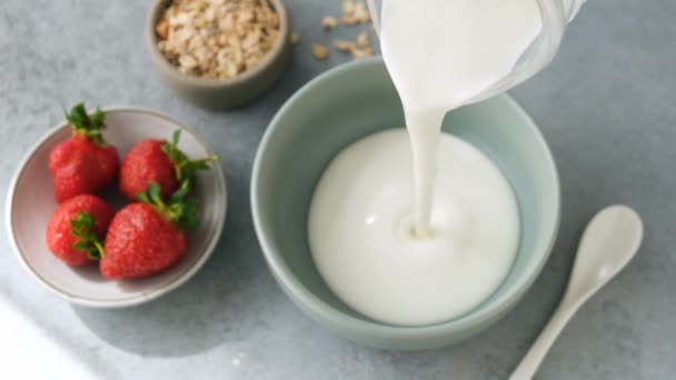 慢动作的天然酸奶倒入碗中 用草莓和意式麦片准备健康早餐酸奶 — 图库视频影像