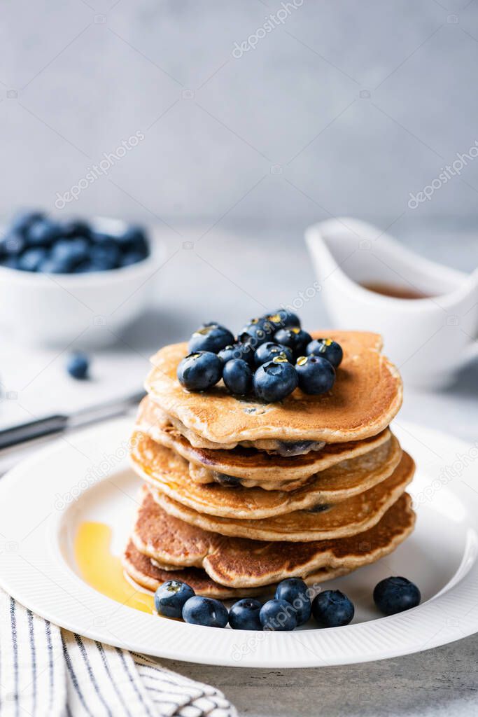 Stack of pancakes with blueberries and maple syrup on white plate, vertical orientation, copy space for text