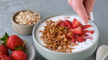 Tahıllı yoğurt, çilek ve chia tohumu. Kadın eli, kahvaltılık sağlıklı yoğurda ağır çekimde chia tohumu ekliyor.