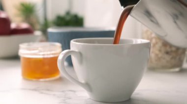 Porselen beyaz fincanın içine dökülen sıcak, sade kahvenin yavaş akışı. Kahvaltı, sabah konsepti.