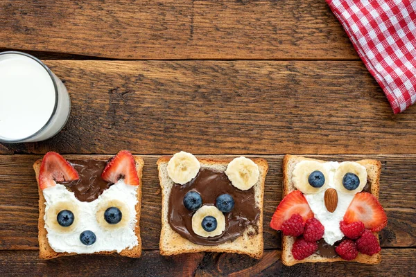 Food art, breakfast toasts shaped as cute funny animals for kids on a wooden table served with glass of milk. Top view. Children\'s food menu