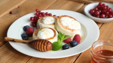 Süzme peynir Syrniki 'ye böğürtlen, bal ve ekşi krema tabakta, ahşap masa arkasında. Tatlı kahvaltı peynirli krep. Geleneksel Rus ve Ukrayna mutfağı