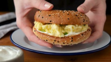 Kadınların elinde çırpılmış yumurtalı susamlı simit sandviçi. Lezzetli kahvaltılık etsiz hamburger.