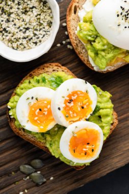 Kızarmış ekmek, avokado püresi ve susam tohumlarıyla süslenmiş yumurta. Sağlıklı avokado açık sandviç.